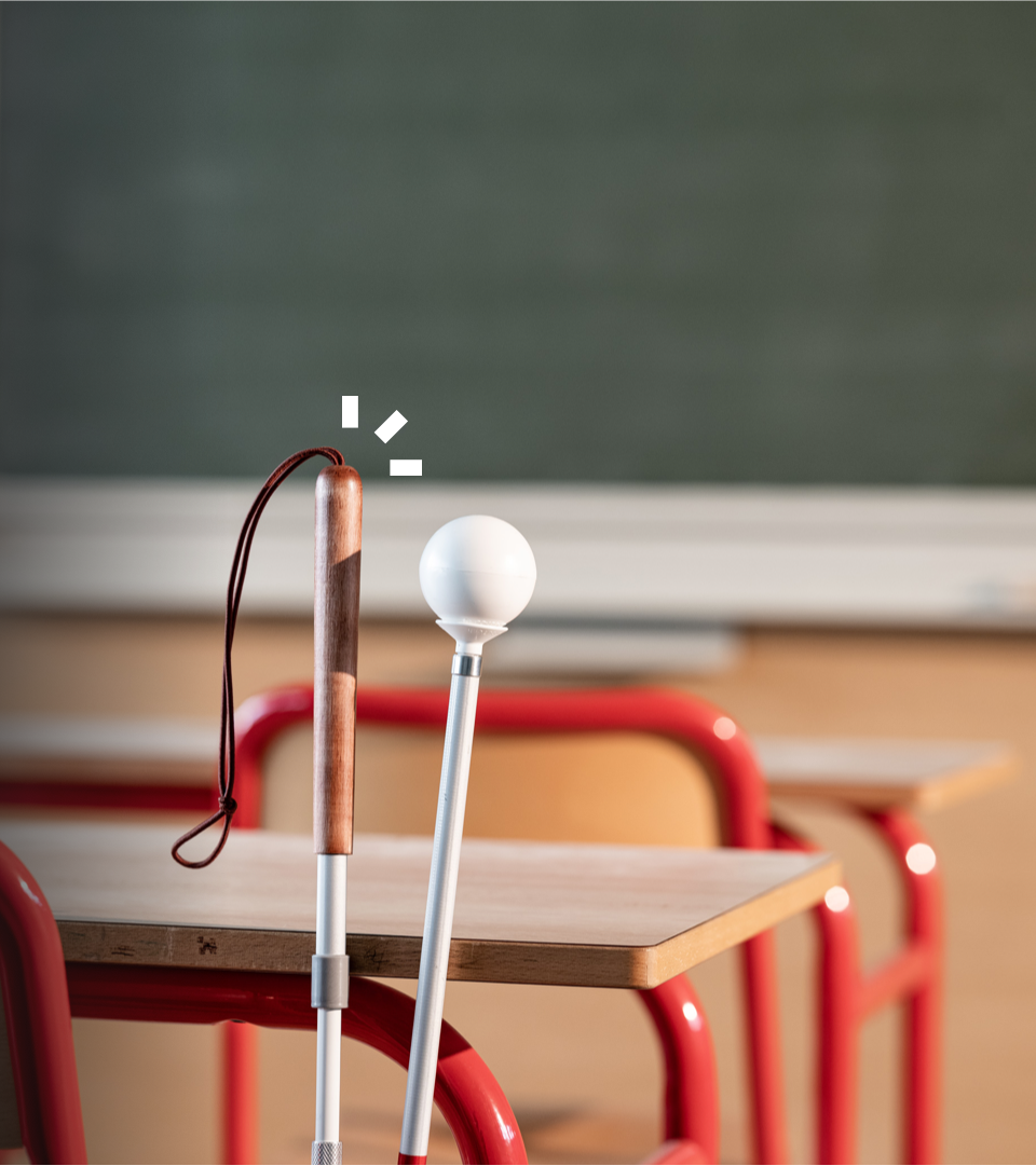 Ein Blindenstock, der in einem Klassenzimmer an eine Schulbank angelehnt ist